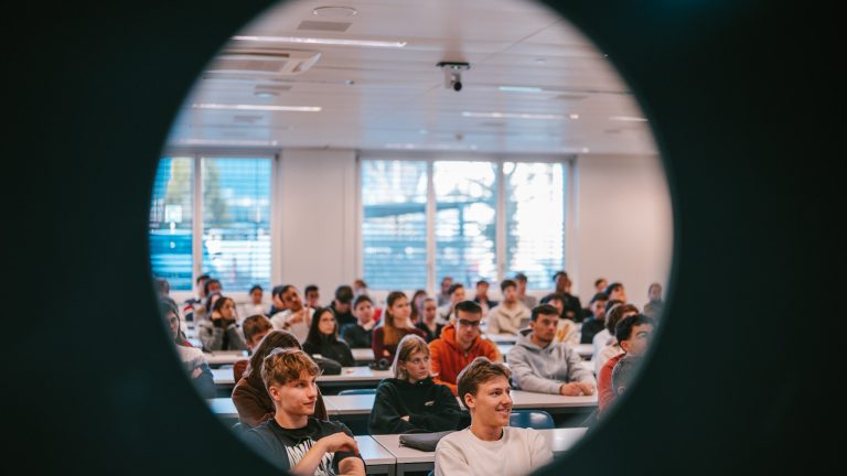 Des étudiantes et des étudiants dans une salle de cours, vu à travers un hublot © DR