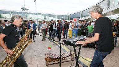 Deux personnes, au premier plan, jouant du saxophone et du piano électrique. Une foule les regardant au second plan