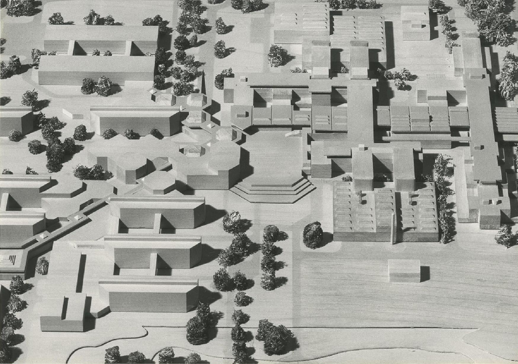 La photographie montre une maquette en bois où l’on retrouve les premiers bâtiments de l’EPFL ainsi que ceux de la deuxième étape. Deux axes se coupent : un axe est-ouest et un axe en diagonale allant du nord-est au sud-ouest. Ils se rejoignent à l’endroit d’une place au centre de la photo. De part et d’autre de ces axes se trouvent les bâtiments.