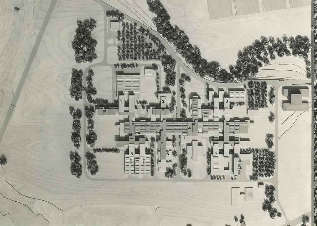 La photographie présente une maquette en bois des bâtiments de la première étape de construction de l’EPFL. On remarque facilement un axe de circulation principal d’où partent les bâtiments tel un peigne.
