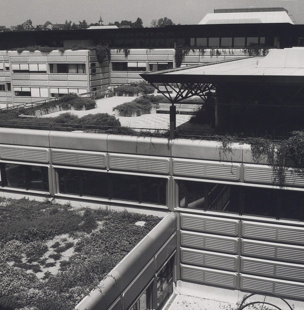 Photographie en noir et blanc d’une terrasse extérieure surélevée de l’EPFL. On observe la présence de végétation.