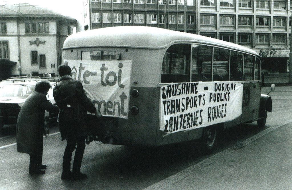 Deux étudiants accrochent contre un bus des banderoles avec des slogans. Ils revendiquent une meilleure liaison entre Lausanne et Dorigny.