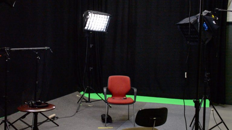 Vue du studio de télévision avec chaise, matériel d’éclairage, rideaux et fond vert.