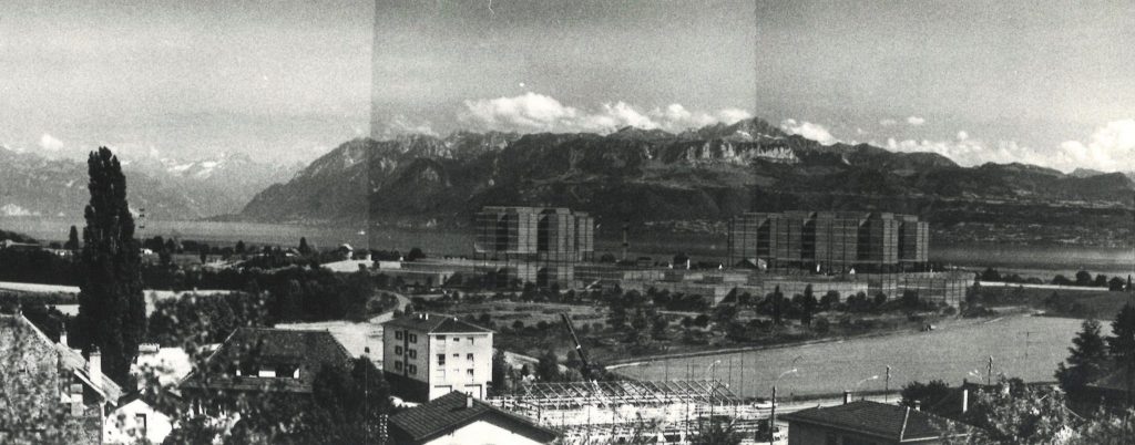 Le volume du projet de 1973 pour la nouvelle EPFL est vu depuis les hauteurs d’Ecublens. Il est représenté dans des tons foncés et se fond dans le paysage.