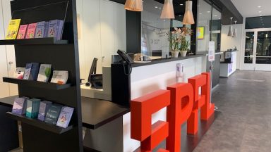 Vue de l'accueil-information à l'EPFL. Un grand logo rouge avec les lettres EPFL est posé devant le bureau d'accueil.