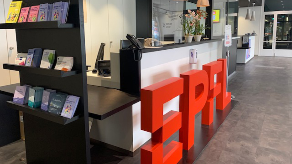Vue de l'accueil-information à l'EPFL. Un grand logo rouge avec les lettres EPFL est posé devant le bureau d'accueil.