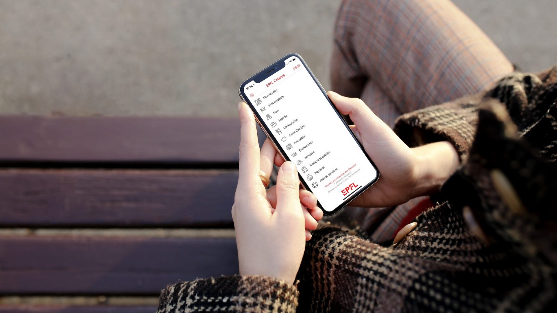 Une personne, assise sur un banc, et tenant dans sa main un smartphone avec l'application EPFL Campus © Pocketcampus