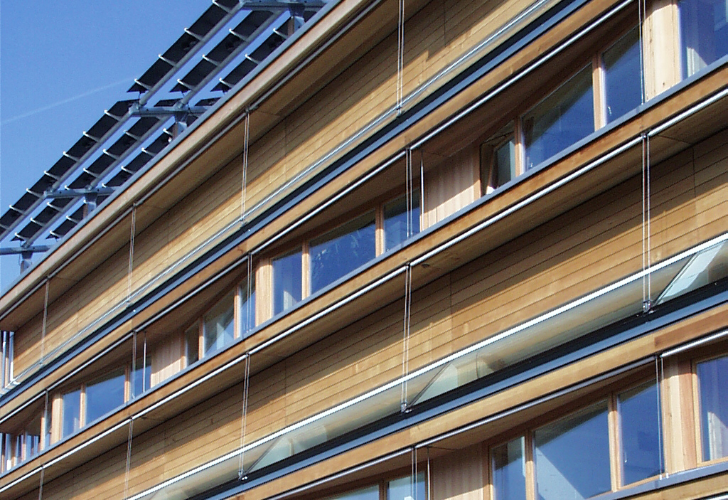 part of the facade of LESO experimental building, wood and windows with smoothly integrated anidolic daylight system as well as pv panels protruding from roof