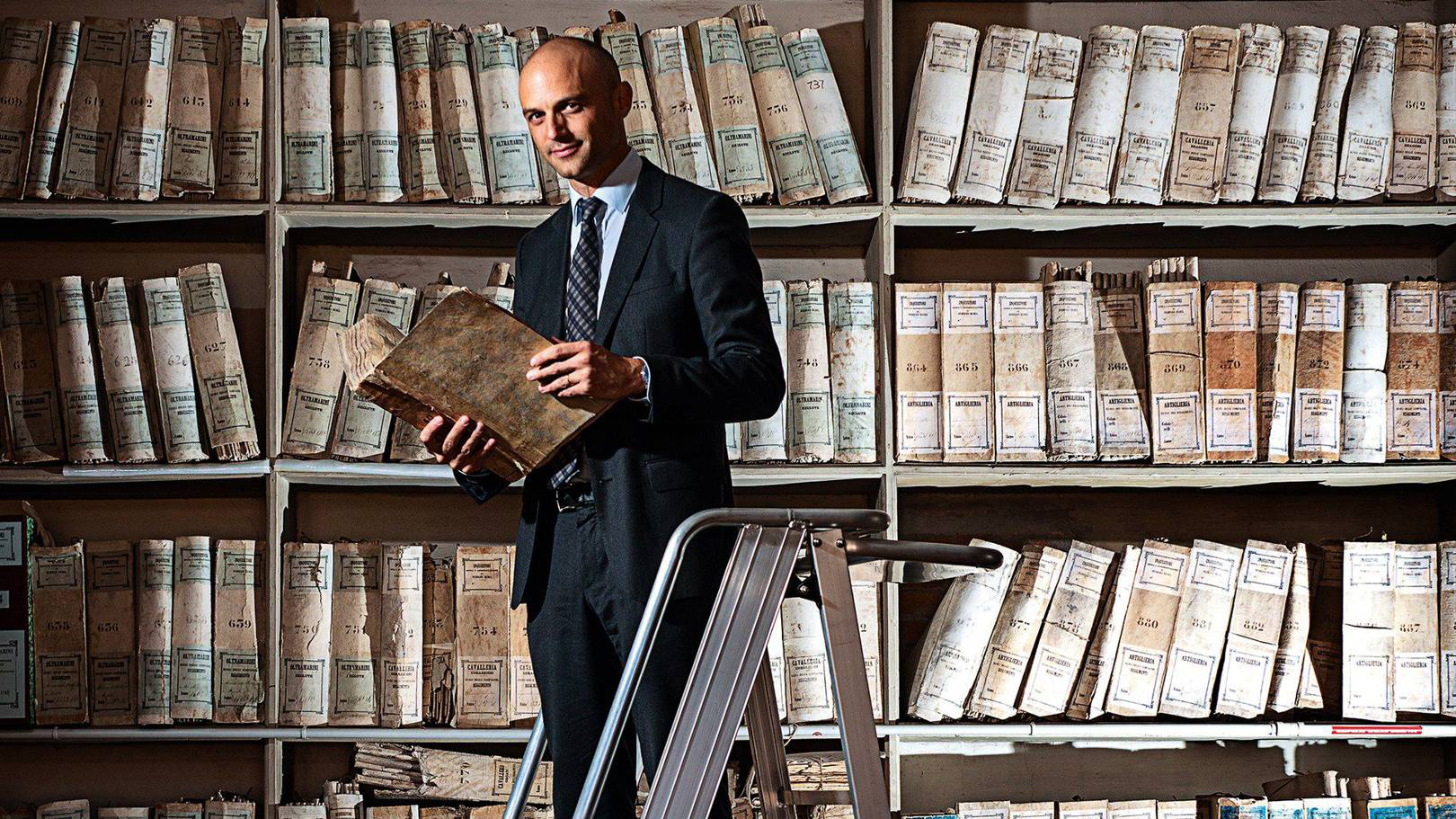 Prof. Kaplan standing on a ladder in front of a wall of archives